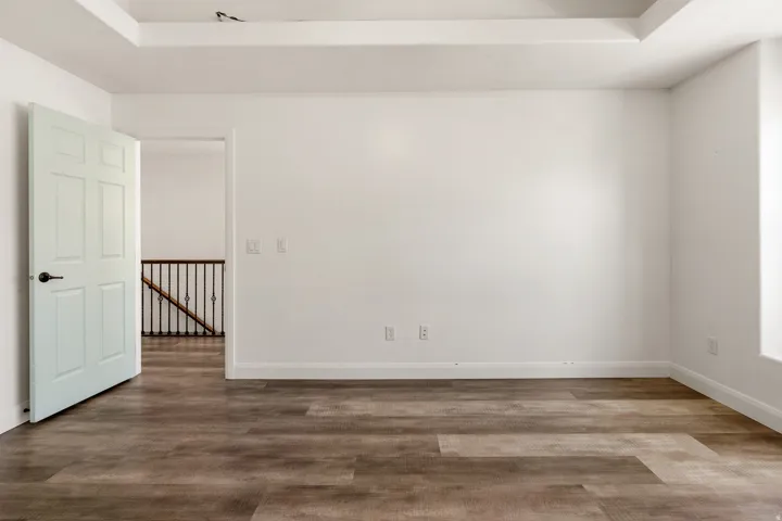 Spacious room featuring wood-finish flooring, white baseboards, and a tray ceiling