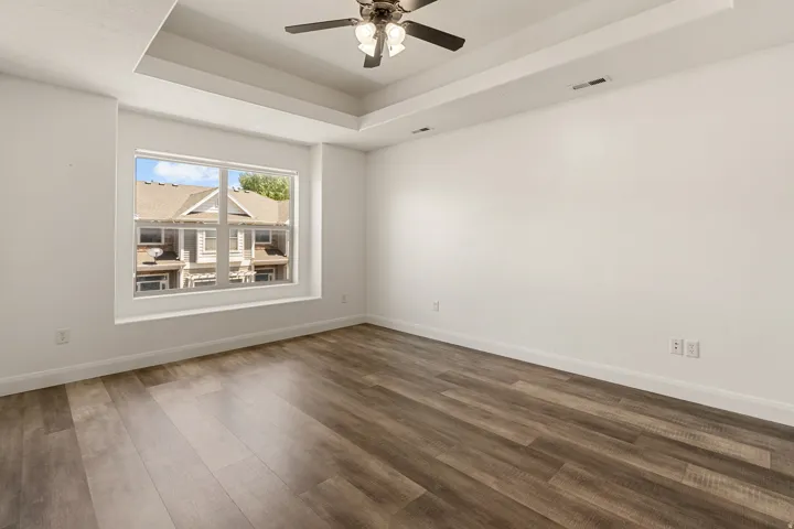 Spacious room featuring wood-finish flooring, a tray ceiling with a ceiling fan, and recessed lighting