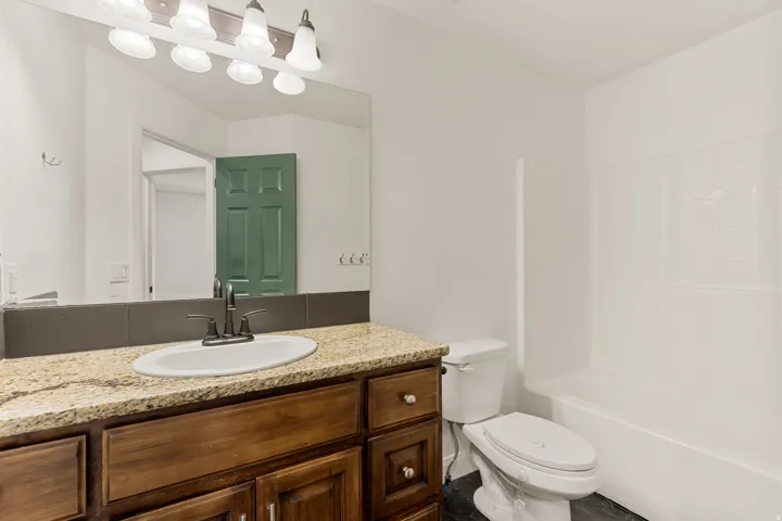 Bathroom featuring a granite-look countertop, dark wood vanity with cabinet storage, oval undermount sink with dark bronze faucet, and a white bathtub with tile surround