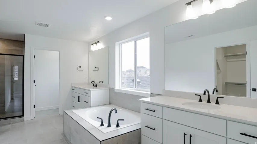 Spa-inspired primary bathroom featuring dual vanities with white cabinetry, quartz countertops, and matte black faucet fixtures