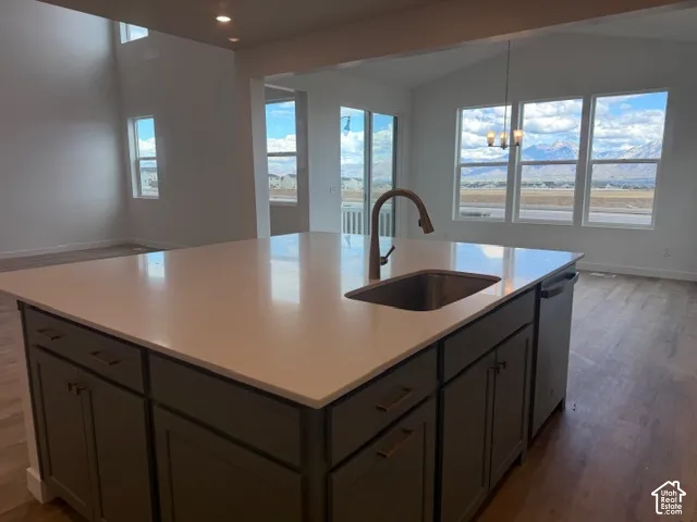 Kitchen island featuring a stone-surface countertop, an integrated stainless steel sink with a high-arch faucet, custom cabinetry with metallic hardware, wood-finish flooring, and expansive windows with mountain scenery