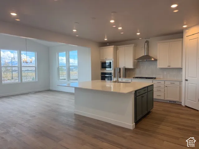 Kitchen featuring wood-finish flooring, white cabinetry, a center island with contrasting base, stone-style countertops, and built-in stainless steel appliances