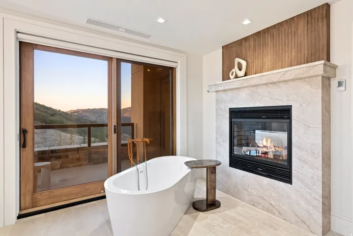 Freestanding soaking tub with a floor-mounted faucet, set against a modern fireplace with a light-toned stone surround and a rich wood accent panel