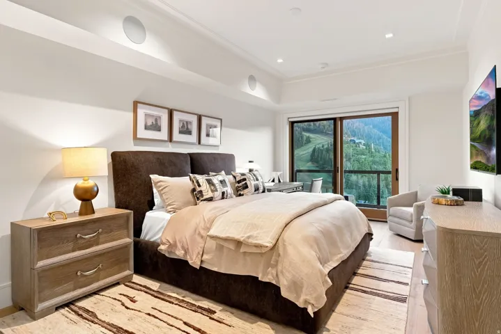 Spacious bedroom featuring wood-finish flooring, a full-height glass sliding door, crown molding, integrated ceiling speakers, and recessed lighting
