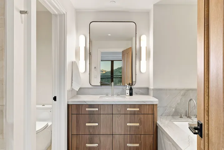 Bathroom vanity featuring a wood-finish cabinet with gold-toned hardware, a white countertop, and an undermount sink