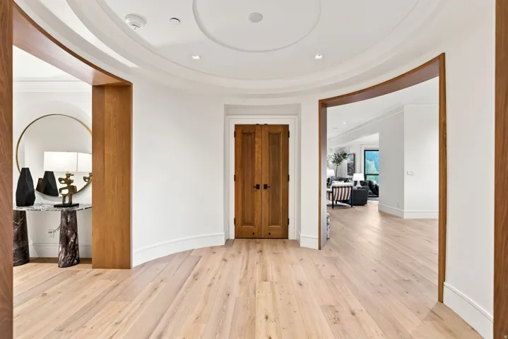 Elegant foyer showcasing curved architectural details, warm wood-finish flooring throughout, and seamless sightlines enhanced by arched doorways with wood-trim framing