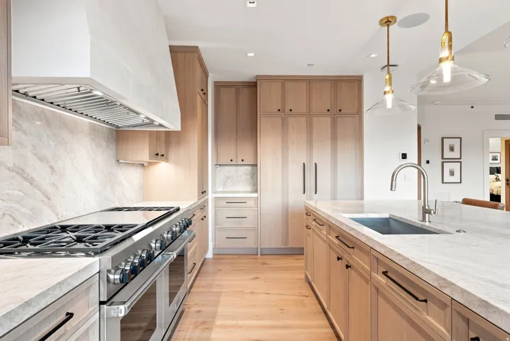 Chef's kitchen featuring custom light wood cabinetry, white marble subway tile backsplash, and marble countertops throughout