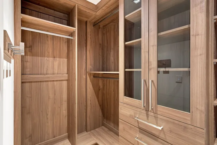 Elegant walk-in closet featuring rich wood cabinetry with glass-front upper storage, multiple shelving units, and polished chrome hardware