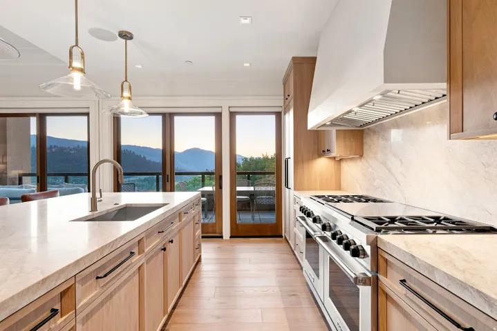 Chef's kitchen featuring light wood cabinetry, white quartz countertops, a six-burner gas range with matching hood, a large center island with prep sink, and pendant lighting