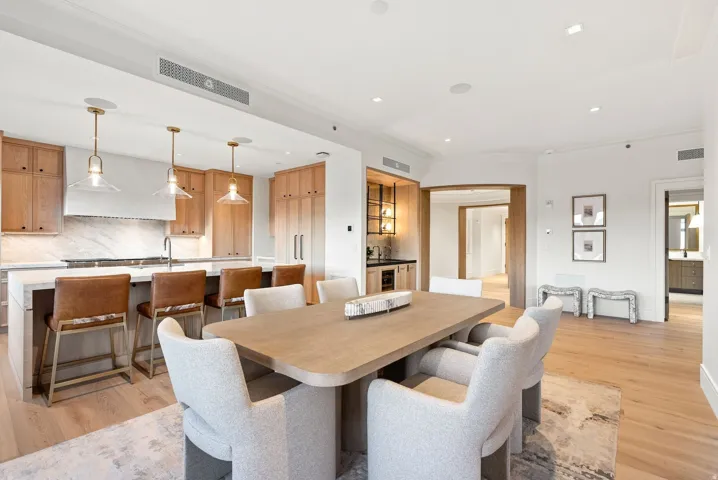 Open-concept dining and kitchen featuring a wood-top dining table with seating for six, natural wood cabinetry, stainless steel appliances, white subway tile backsplash, pendant lighting, hardwood flooring throughout, and abundant recessed ceiling lightin