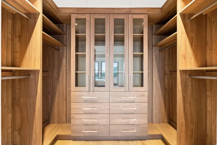 Custom wood-finish cabinetry featuring glass-front doors, built-in drawers, open shelving, and hanging rods
