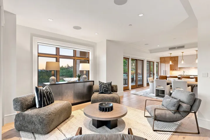 Open-concept living area featuring curved upholstered seating, a round wood-finish coffee table with black base, and hardwood flooring throughout