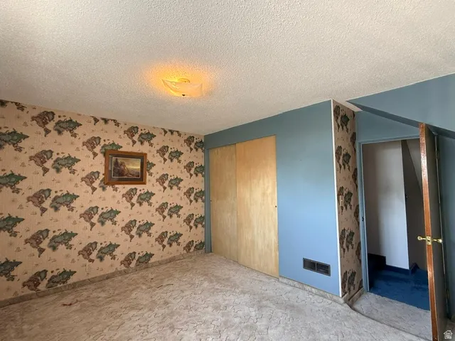 Spacious bedroom showcasing decorative floral wallpaper, wood-finish door, blue accent wall, recessed ceiling lighting, and neutral carpeting throughout