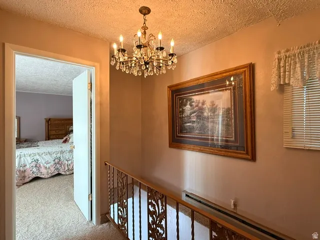 Elegant upper-level hallway showcasing warm apricot walls, ornate crystal chandelier with candle-style lighting, decorative framed artwork, wooden stair railing with turned balusters, and access to additional bedroom space
