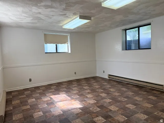 Spacious room featuring patterned tile flooring, white walls with wainscoting, two windows, and fluorescent overhead lighting
