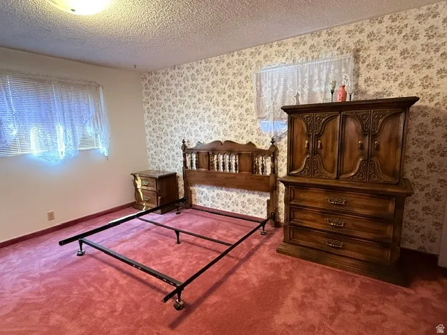 Bedroom featuring textured red carpeting, a decorative floral wallpaper accent wall, and a window with blinds