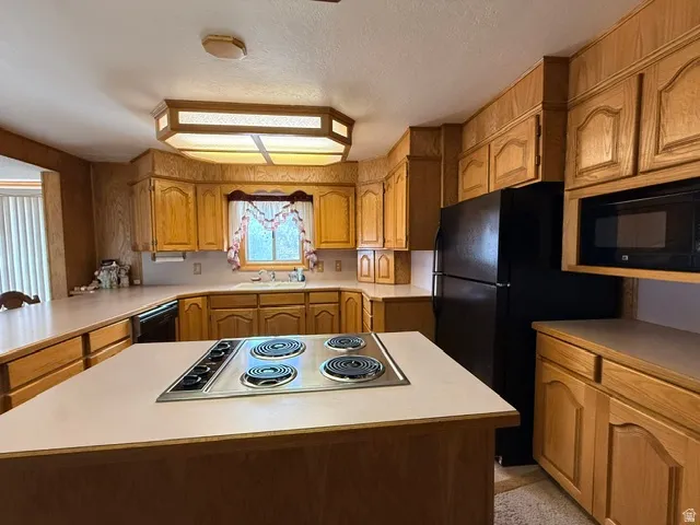Kitchen featuring wood-finish cabinetry, a built-in cooktop, a black refrigerator, a wall-mounted microwave, and a double basin sink