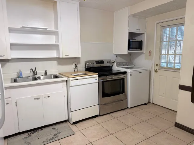 Efficient kitchen layout featuring white cabinetry with open shelving, stainless steel range and refrigerator, ceramic tile flooring, and direct access to exterior door