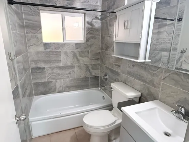 Updated Bathroom Featuring Tile Surround Walls, Alcove Tub with Shower Enclosure, Floating Vanity with Rectangular Sink, Toilet, and Recessed Medicine Cabinet Storage