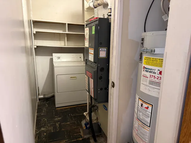 Utility closet featuring stackable washer/dryer unit, built-in shelving, water heater with safety labels, and organized mechanical systems