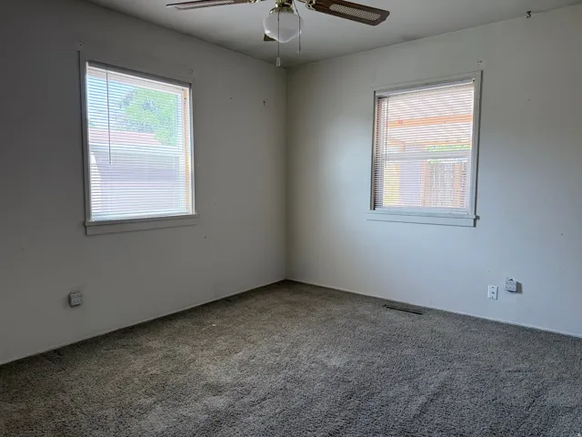 Carpeted room with a ceiling fan light fixture, two windows with blinds, and white wall finishes