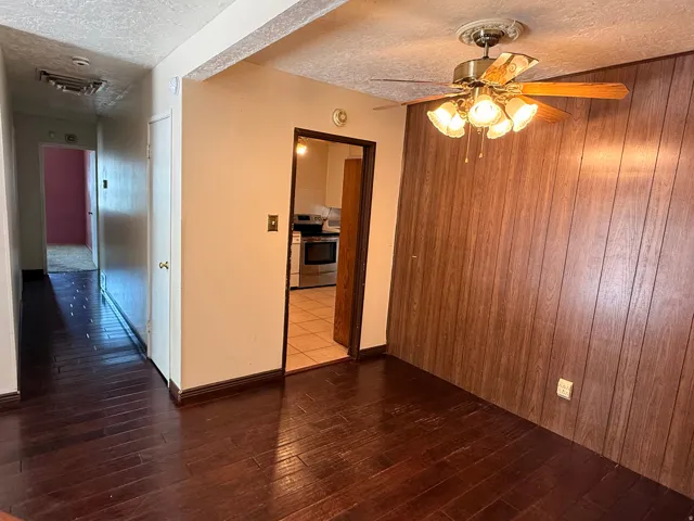 Spacious living area showcasing rich wood-finish flooring, warm neutral walls, and wood-paneled accent wall