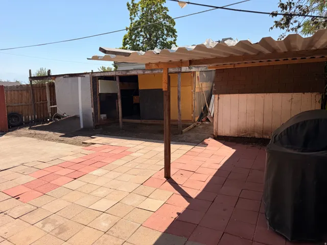 Spacious outdoor patio area featuring terracotta tile flooring, wooden pergola shade structure, and mature landscape trees