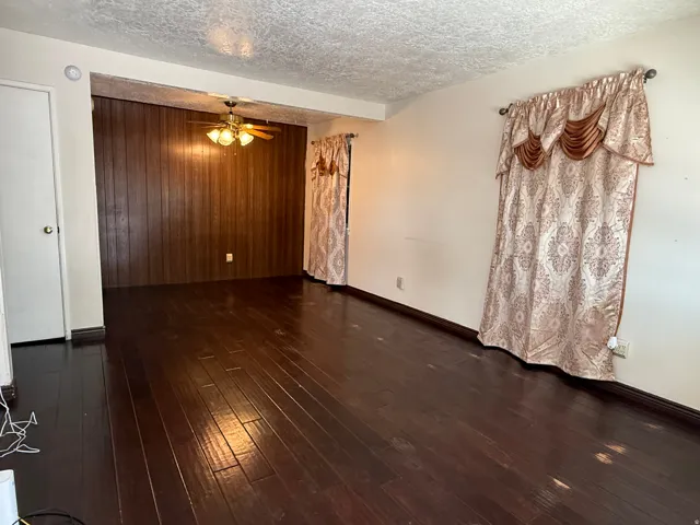 Spacious living area showcasing rich wood-finish flooring, ceiling fan with integrated lighting, and elegant fabric window treatments