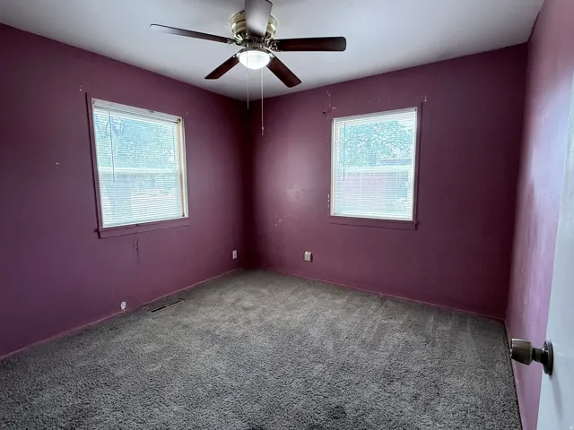 Carpeted room featuring dual windows, a ceiling fan with integrated lighting, and a white door with a bronze-toned doorknob