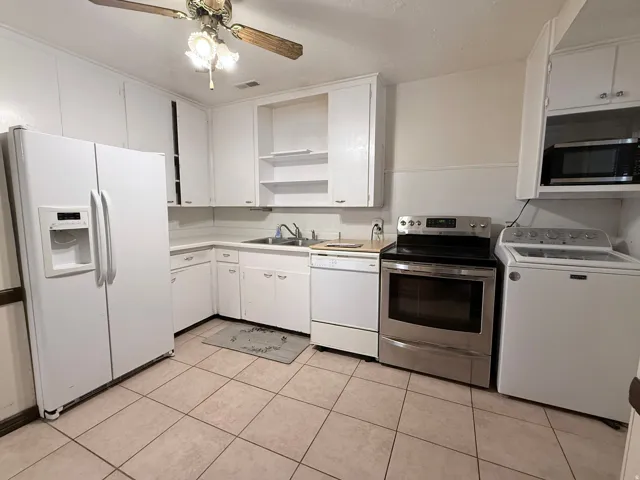 Spacious kitchen featuring white cabinetry with ample storage, stainless steel appliances including a slide-in range and microwave, tile flooring, and a ceiling fan with integrated lighting