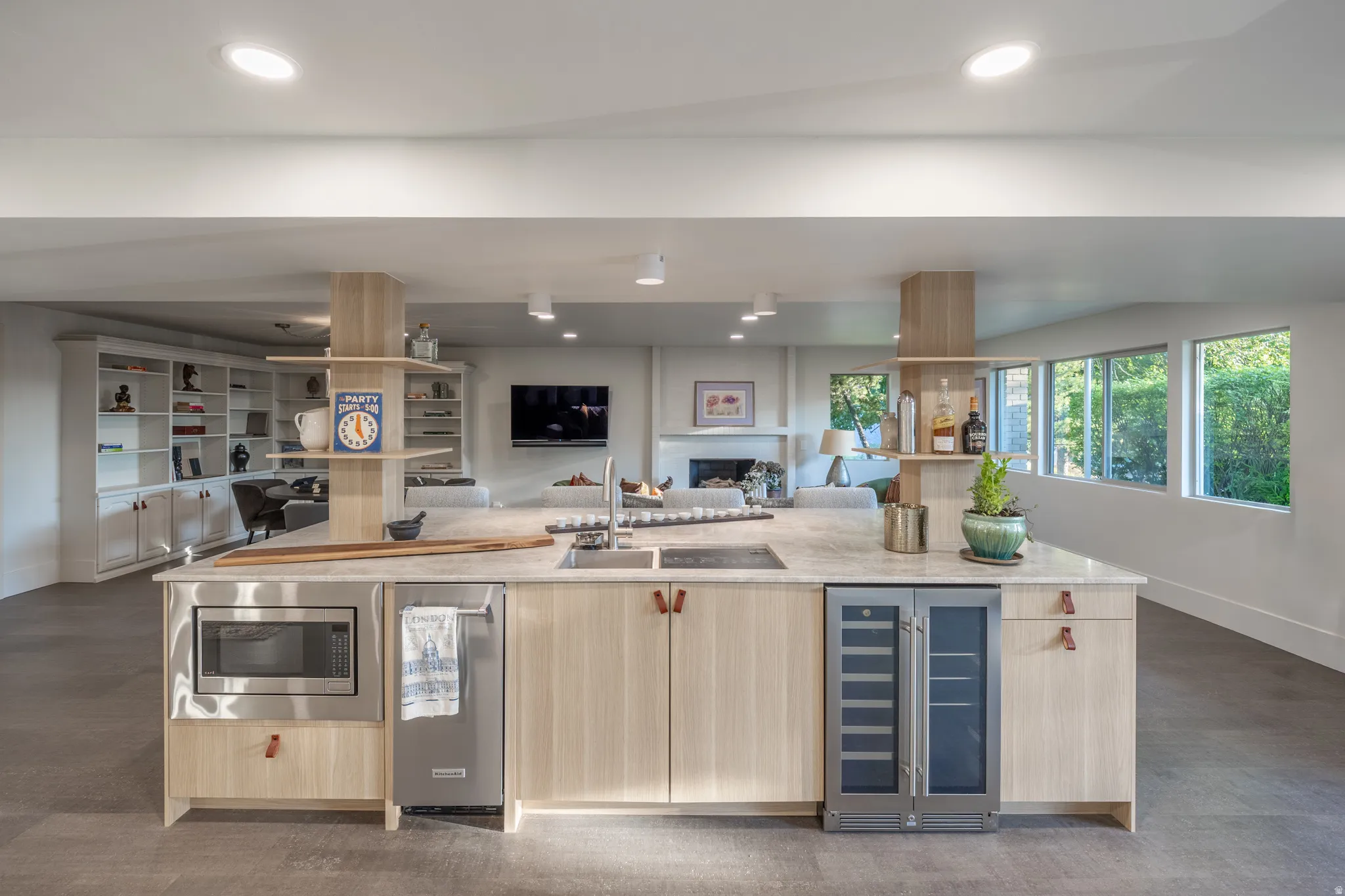 Open-concept lower level featuring a large kitchen island with light wood-finish cabinetry, stainless steel microwave, integrated dishwasher, and beverage cooler