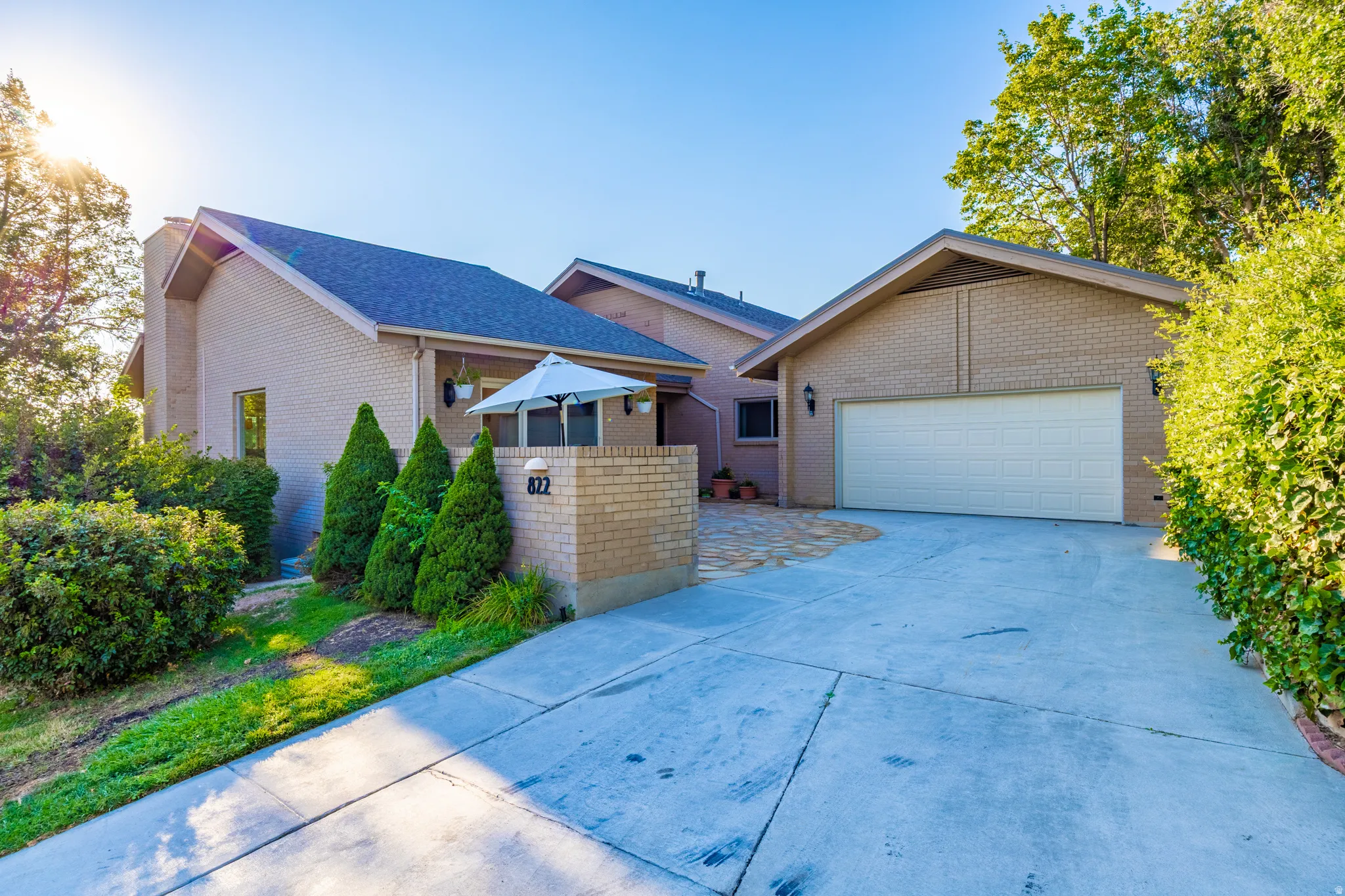 Brick exterior residence featuring a spacious concrete driveway, two-car attached garage with white paneled door, and mature landscaping with evergreen shrubs