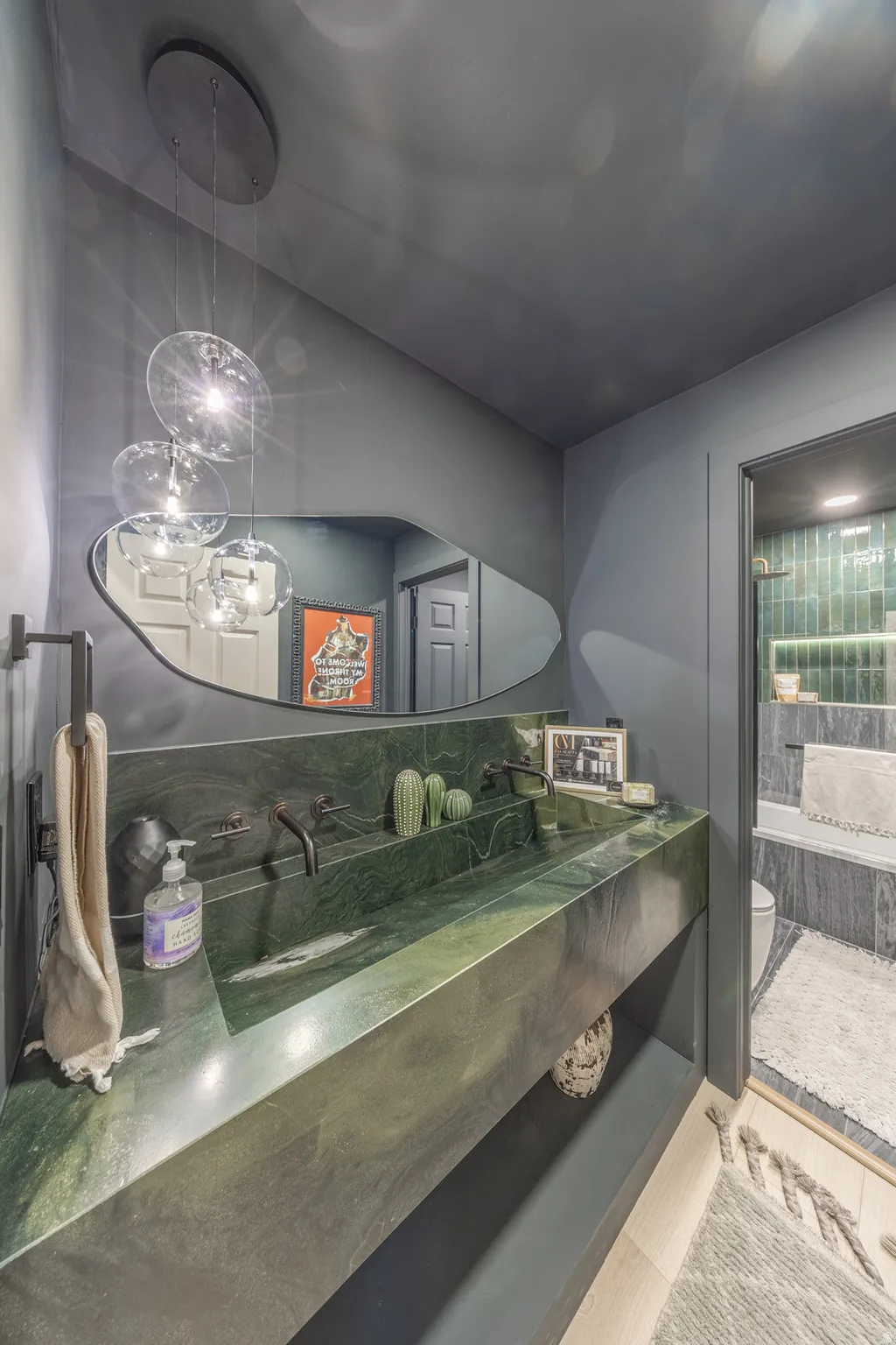 Modern bathroom featuring a striking green stone vanity with integrated dual sinks and wall-mounted bronze faucets