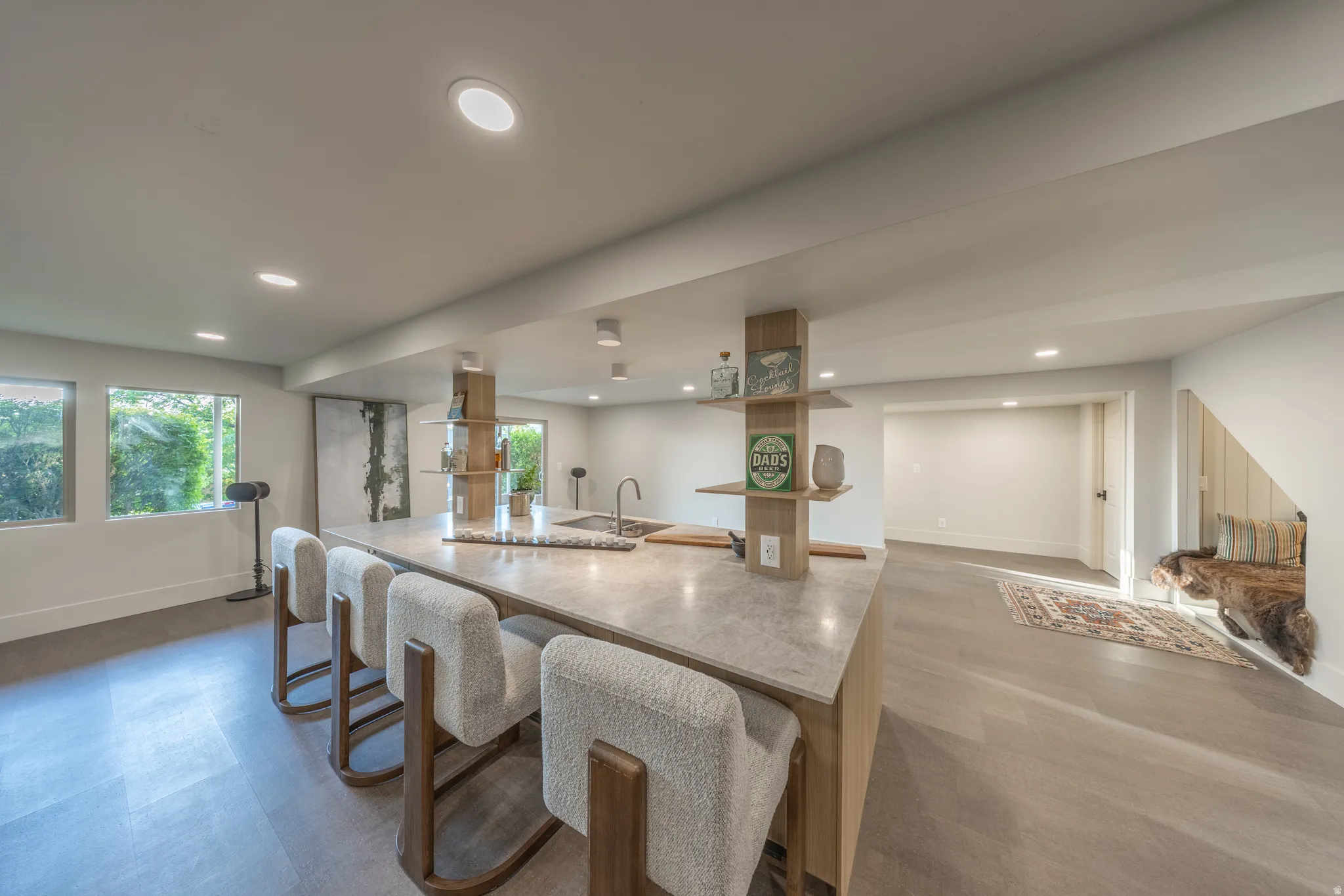 Open-concept kitchen and living area showcasing a waterfall-edge island with seating for three, stainless steel appliances, white cabinetry, and polished concrete countertops