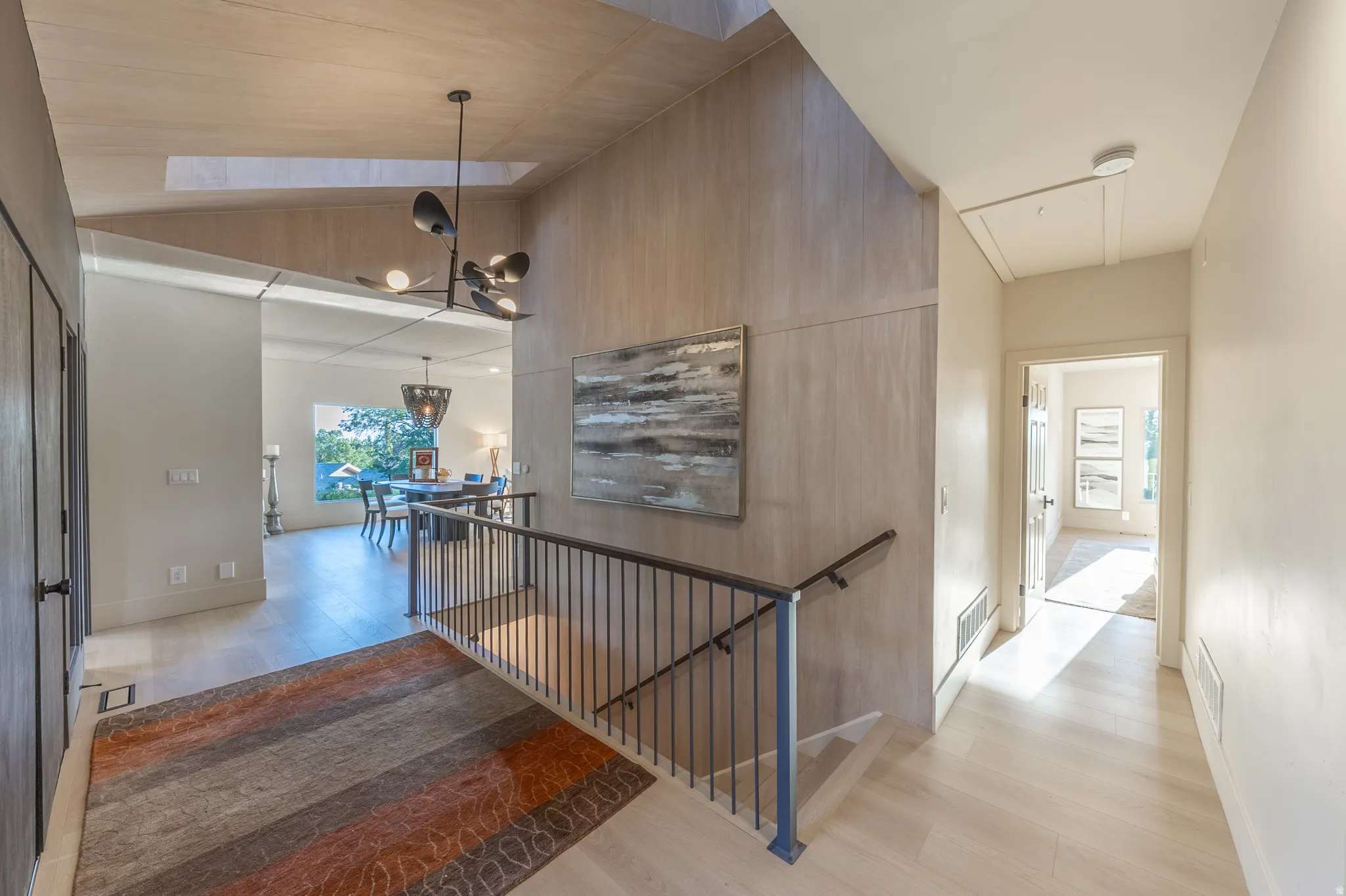 Modern open-concept foyer featuring soaring vaulted ceilings with wood-finish paneling, a floating staircase with black metal railings, polished concrete flooring, and abundant natural light from clerestory windows
