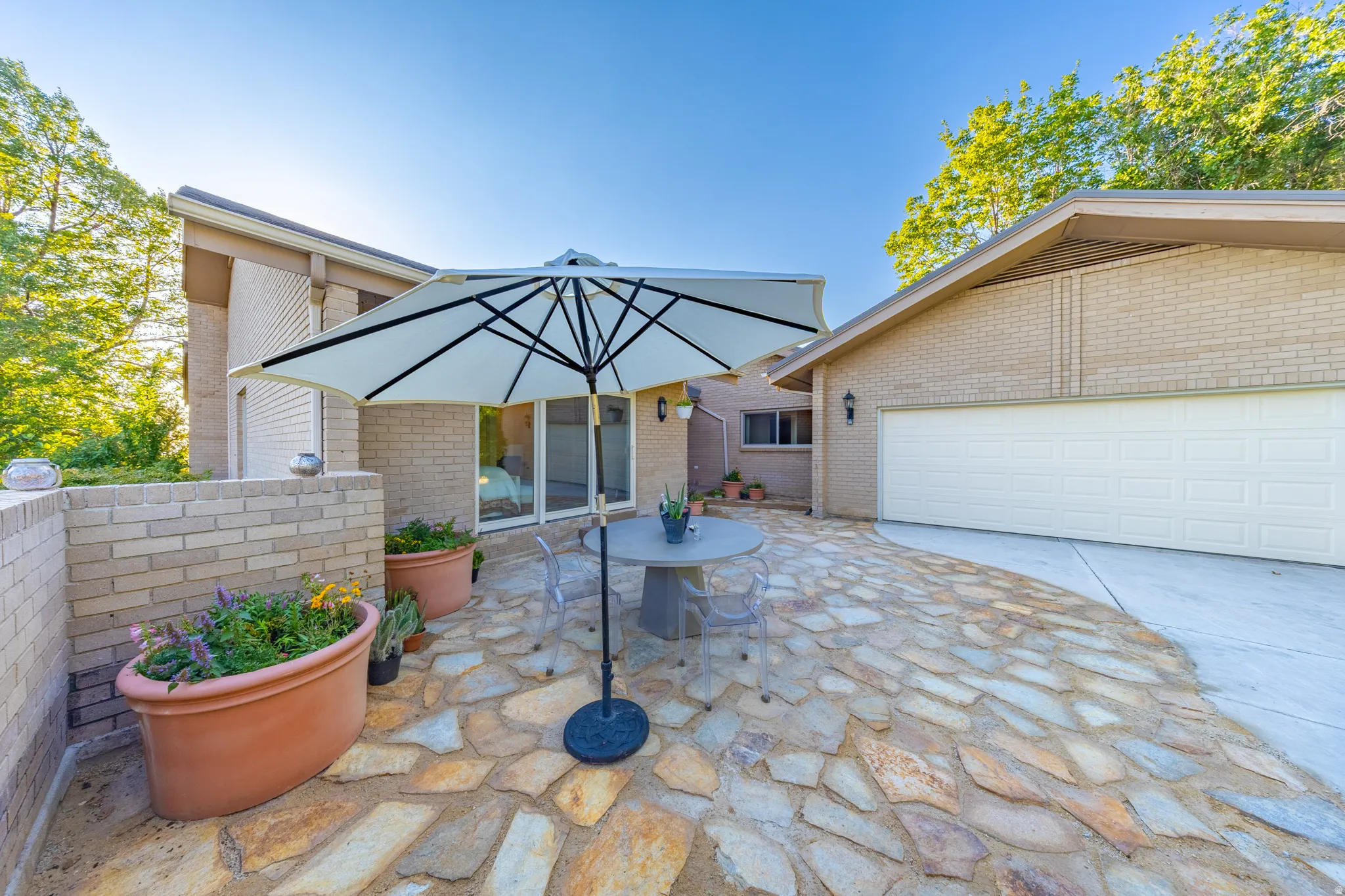 Exterior patio featuring natural stone pavers, a brick retaining wall, and a light-colored brick facade