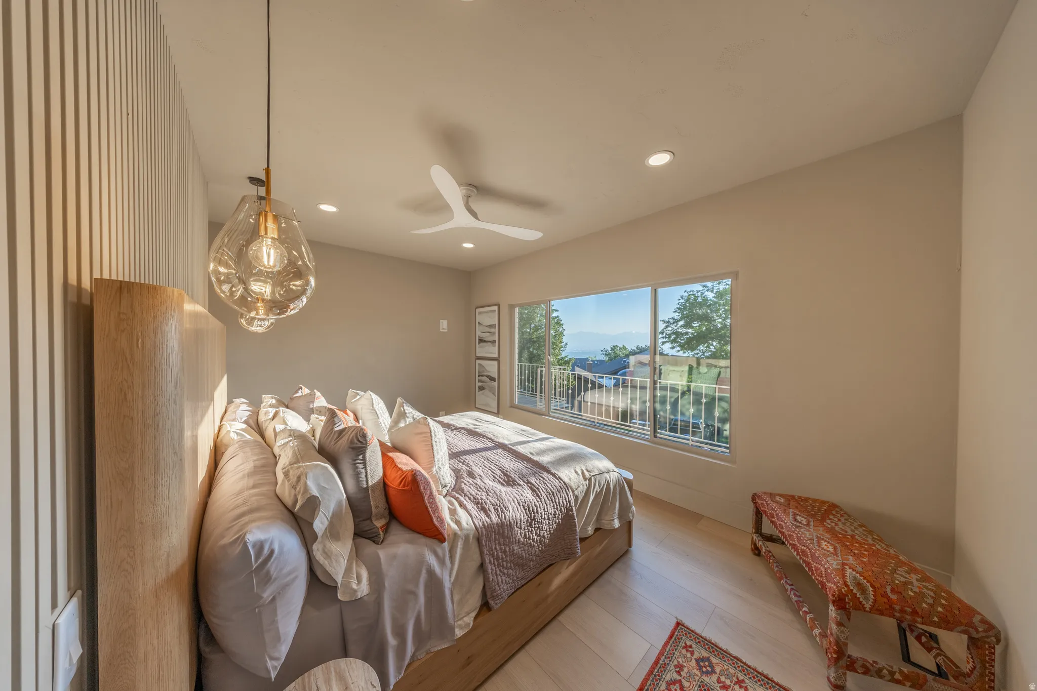 Bright bedroom showcasing warm neutral walls, wood-finish flooring, and a large picture window with outdoor scenery