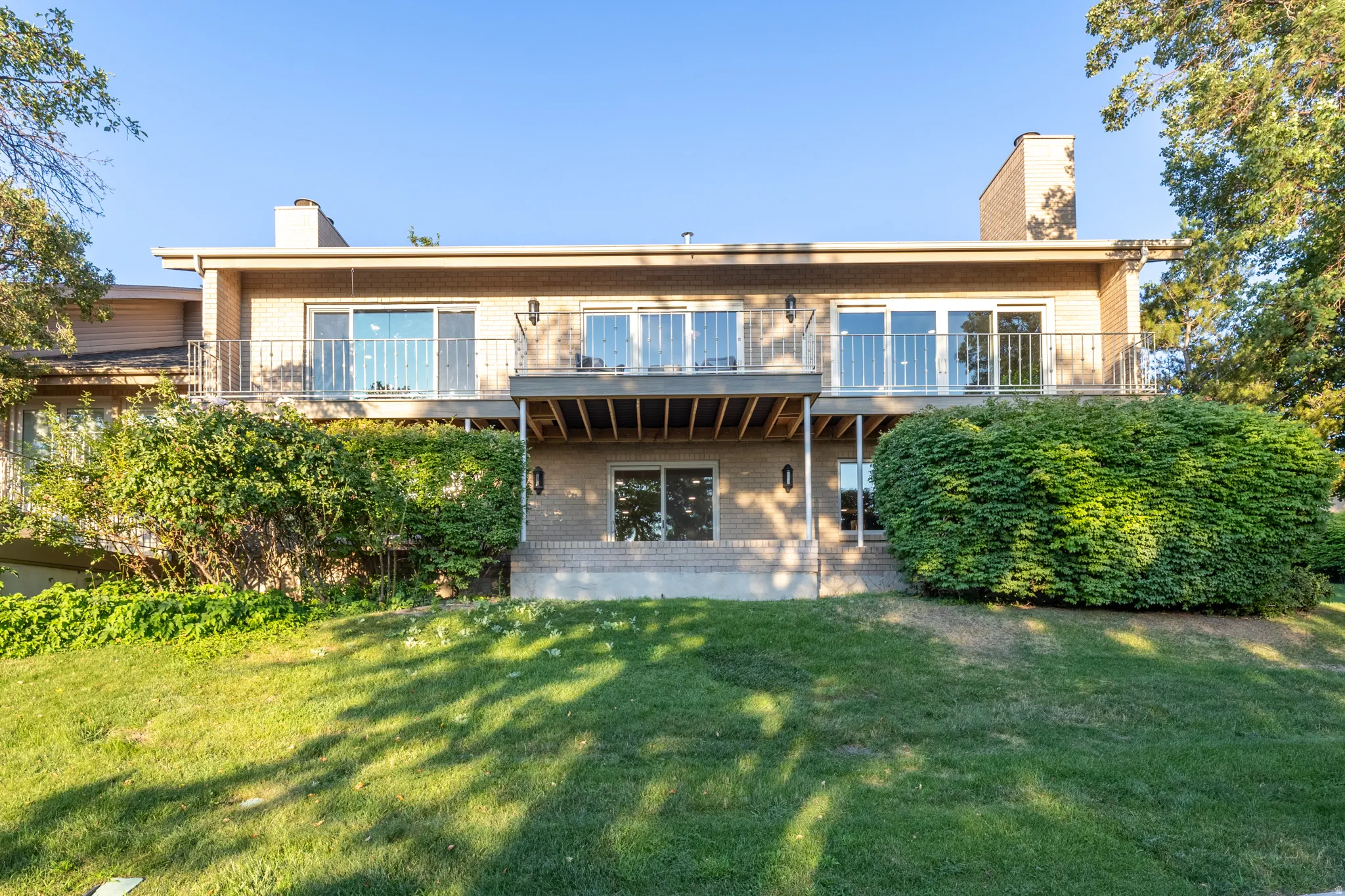 Modern multi-level residence featuring a substantial rear elevation with expansive glazing, concrete terrace, and mature landscaping