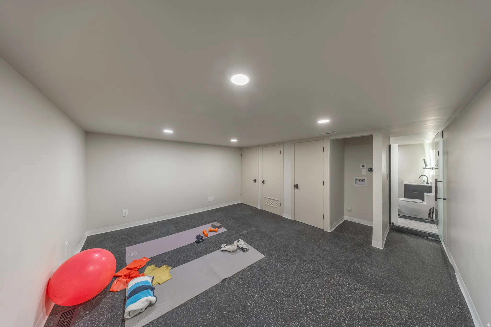 Finished basement recreation room featuring dark gray carpeting, recessed ceiling lighting, and multiple closeted storage areas