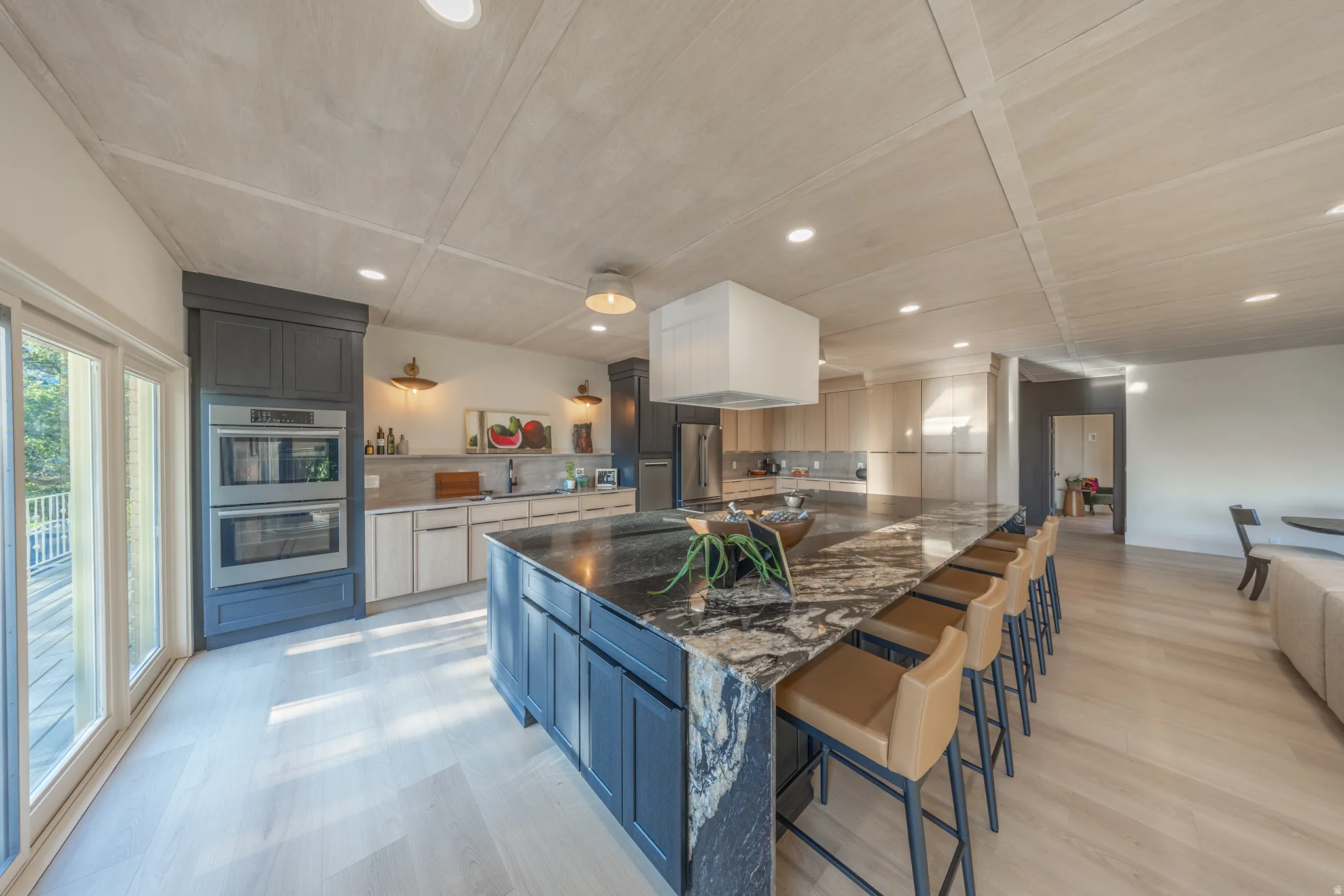 Gourmet kitchen featuring a large waterfall-edge island with seating for multiple guests, dual built-in wall ovens, stainless steel appliances, and quartz countertops