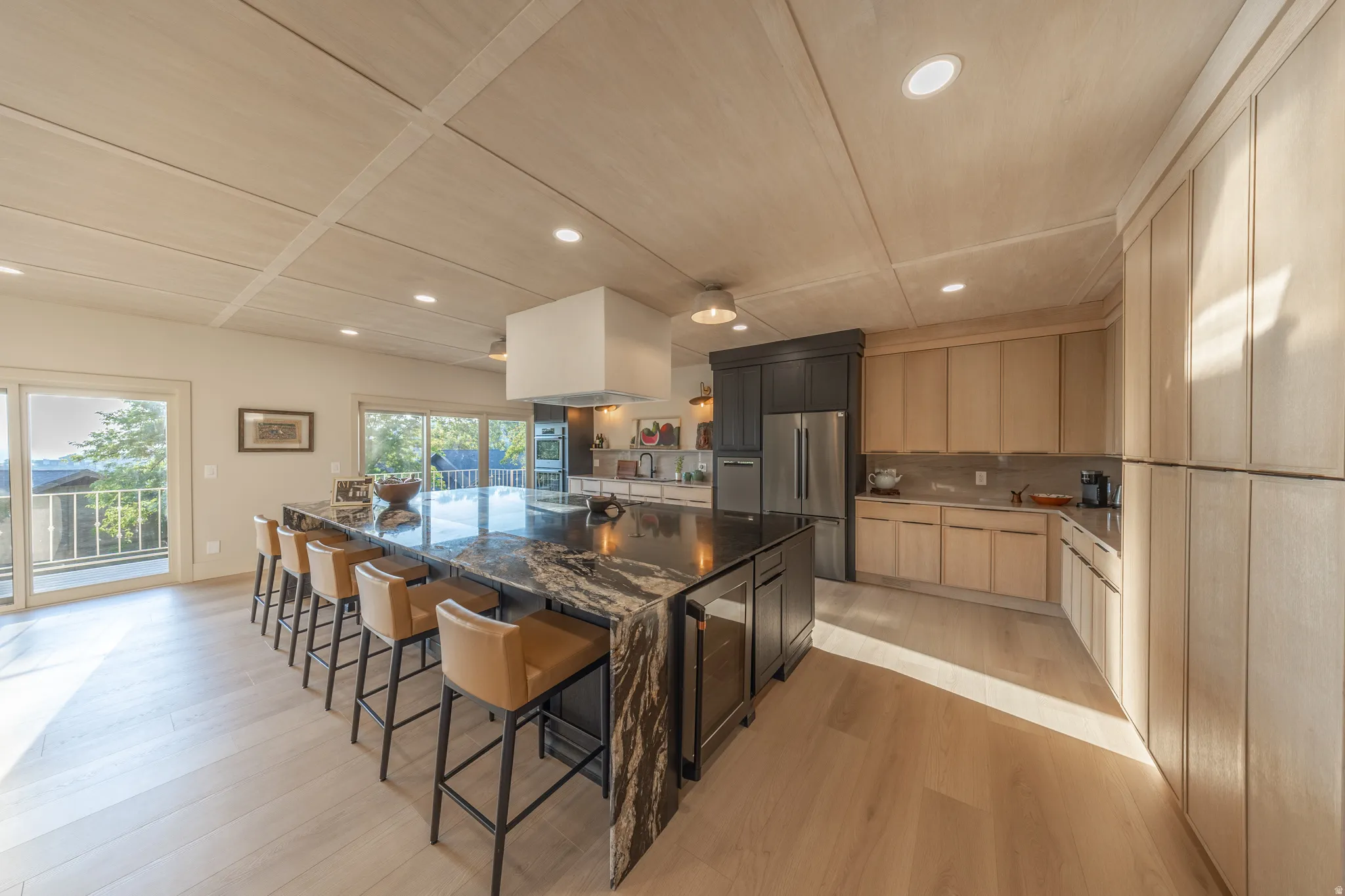 Chef's kitchen featuring a large center island with waterfall edge countertop and seating for multiple guests, professional-grade stainless steel appliances, custom cabinetry with ample storage, recessed and pendant lighting throughout, and direct access