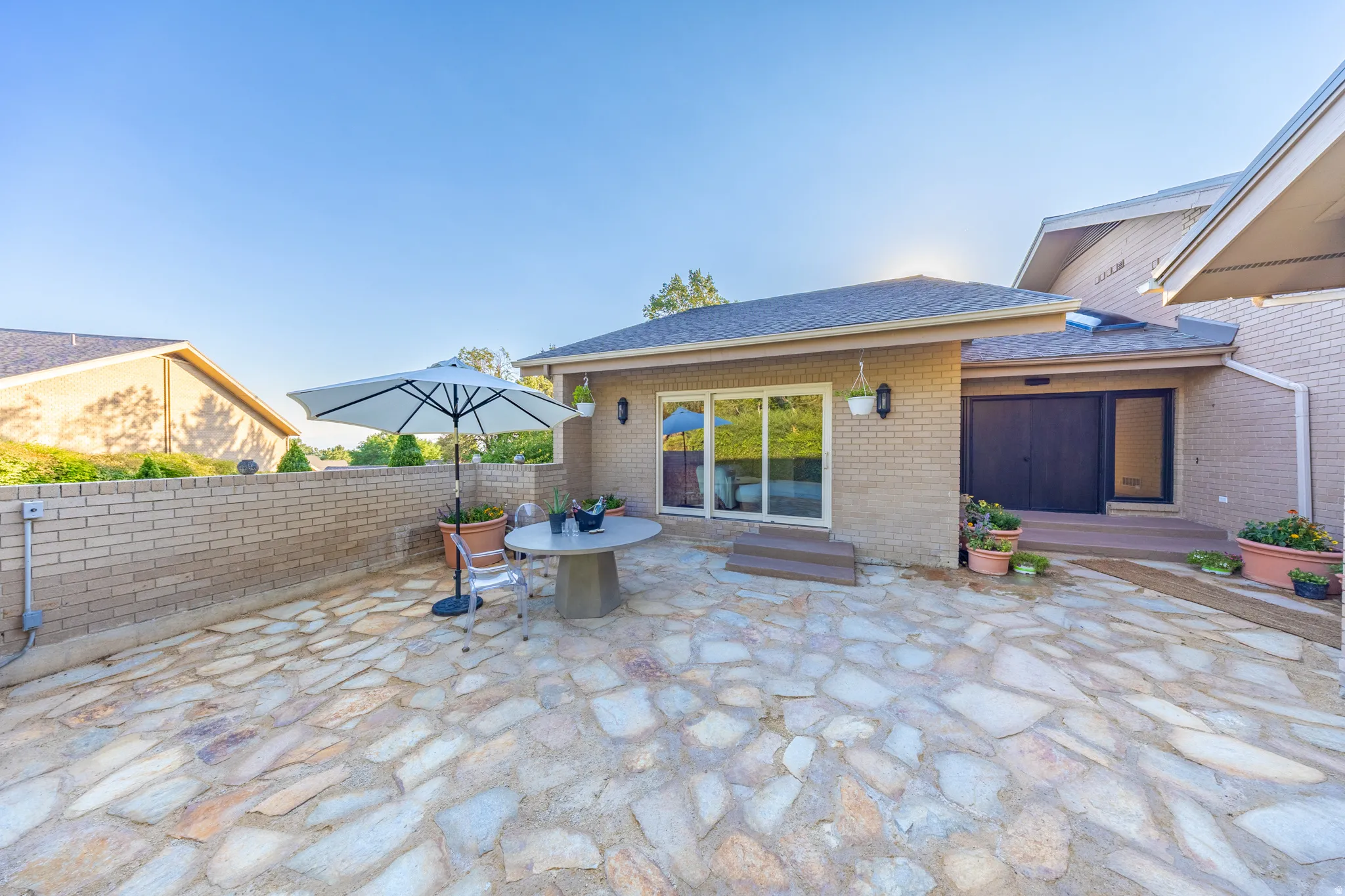 Spacious patio featuring irregular stone paving, a low brick retaining wall, and direct access to the interior via sliding glass doors and a dark-framed entry