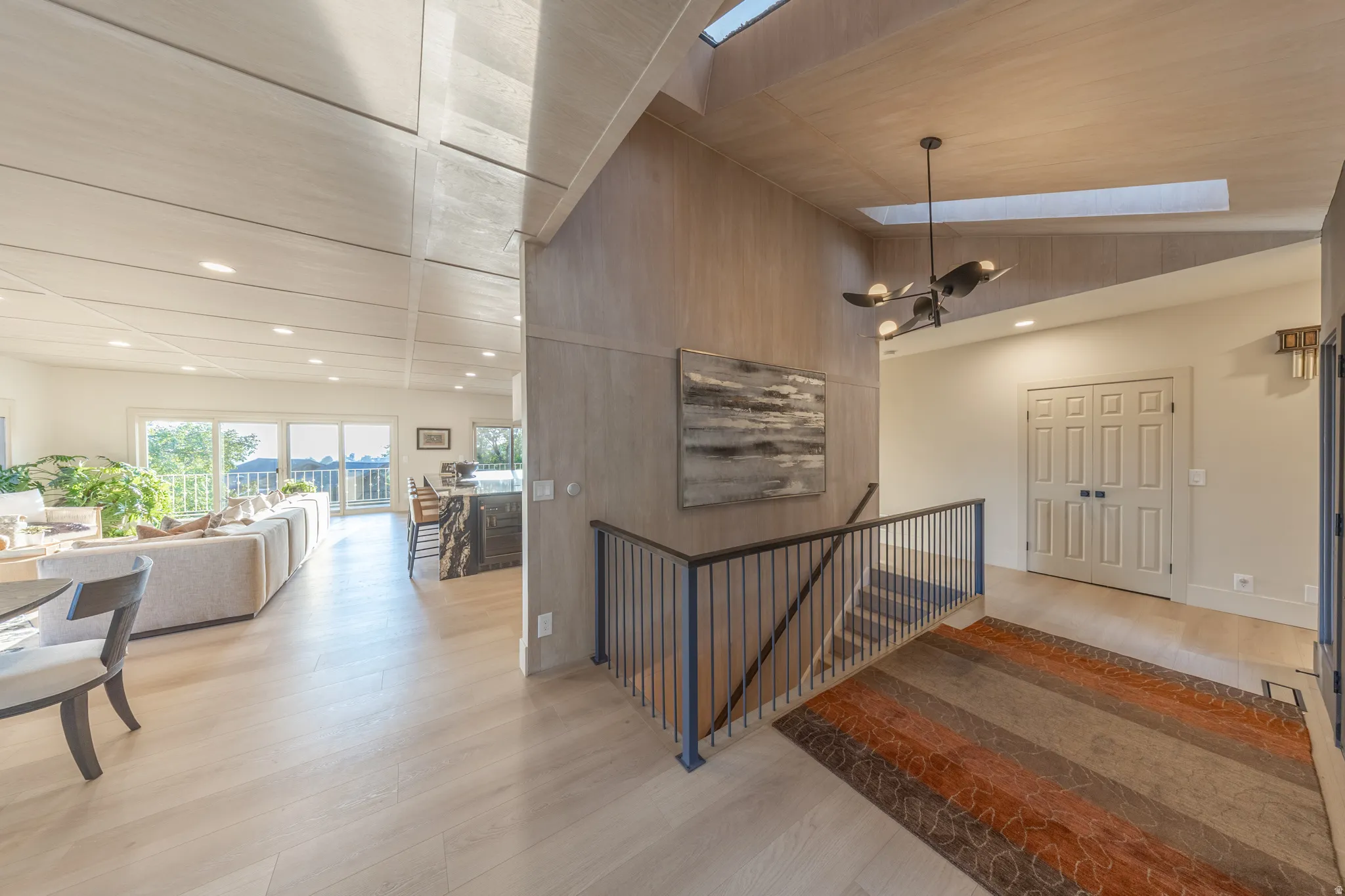 Dramatic two-story foyer showcasing soaring ceilings with skylights and exposed wood beams, anchored by a modern metal railing staircase