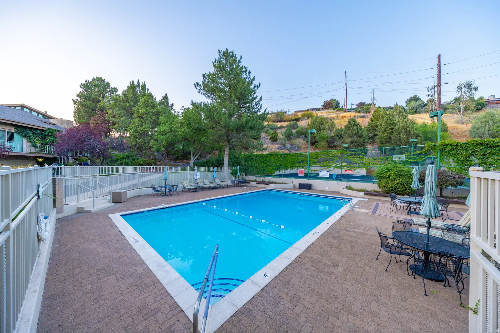 Resort-style swimming pool with crystal-blue water and surrounding paver decking, complemented by mature landscaping, hillside backdrop, and integrated lounge seating areas