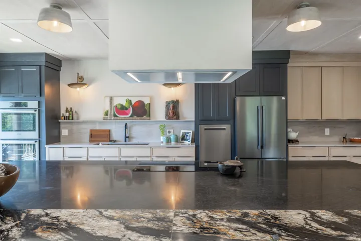 Kitchen featuring a large island with dark stone countertop, integrated stainless steel appliances, custom cabinetry, and pendant lighting