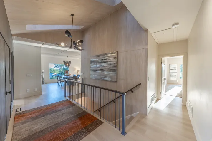 Modern open-concept foyer featuring soaring vaulted ceilings with wood-finish paneling, a floating staircase with black metal railings, polished concrete flooring, and abundant natural light from clerestory windows