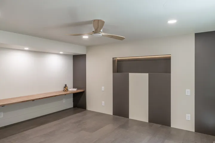 Wood-finish flooring, built-in desk with wood-finish surface, recessed ceiling lighting, modern ceiling fan, and architectural wall paneling