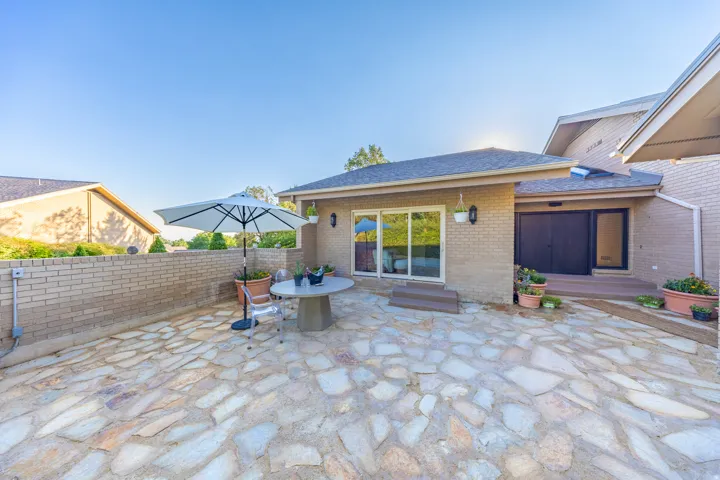 Spacious patio featuring irregular stone paving, a low brick retaining wall, and direct access to the interior via sliding glass doors and a dark-framed entry