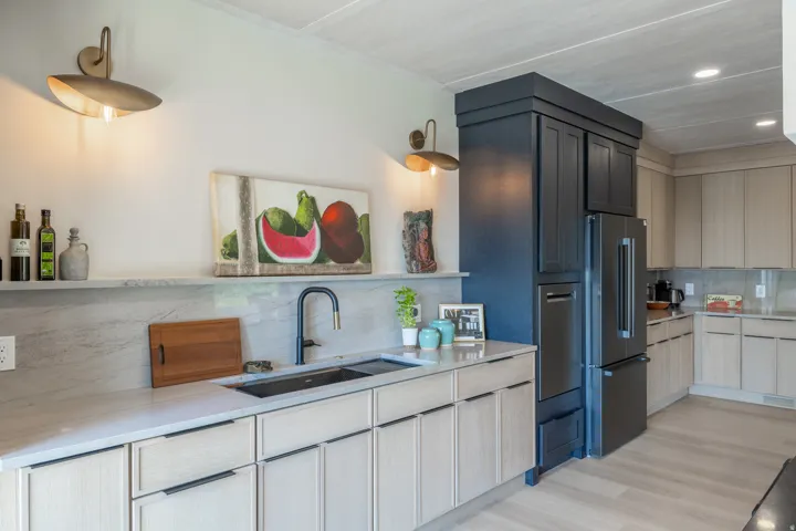 Integrated black stainless steel refrigerator and dishwasher, light wood-finish cabinetry, light stone countertops, and a black single-basin sink with a matte black faucet