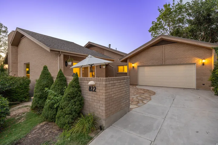 Brick exterior featuring a multi-level roofline, attached garage, and a private patio with a low brick wall